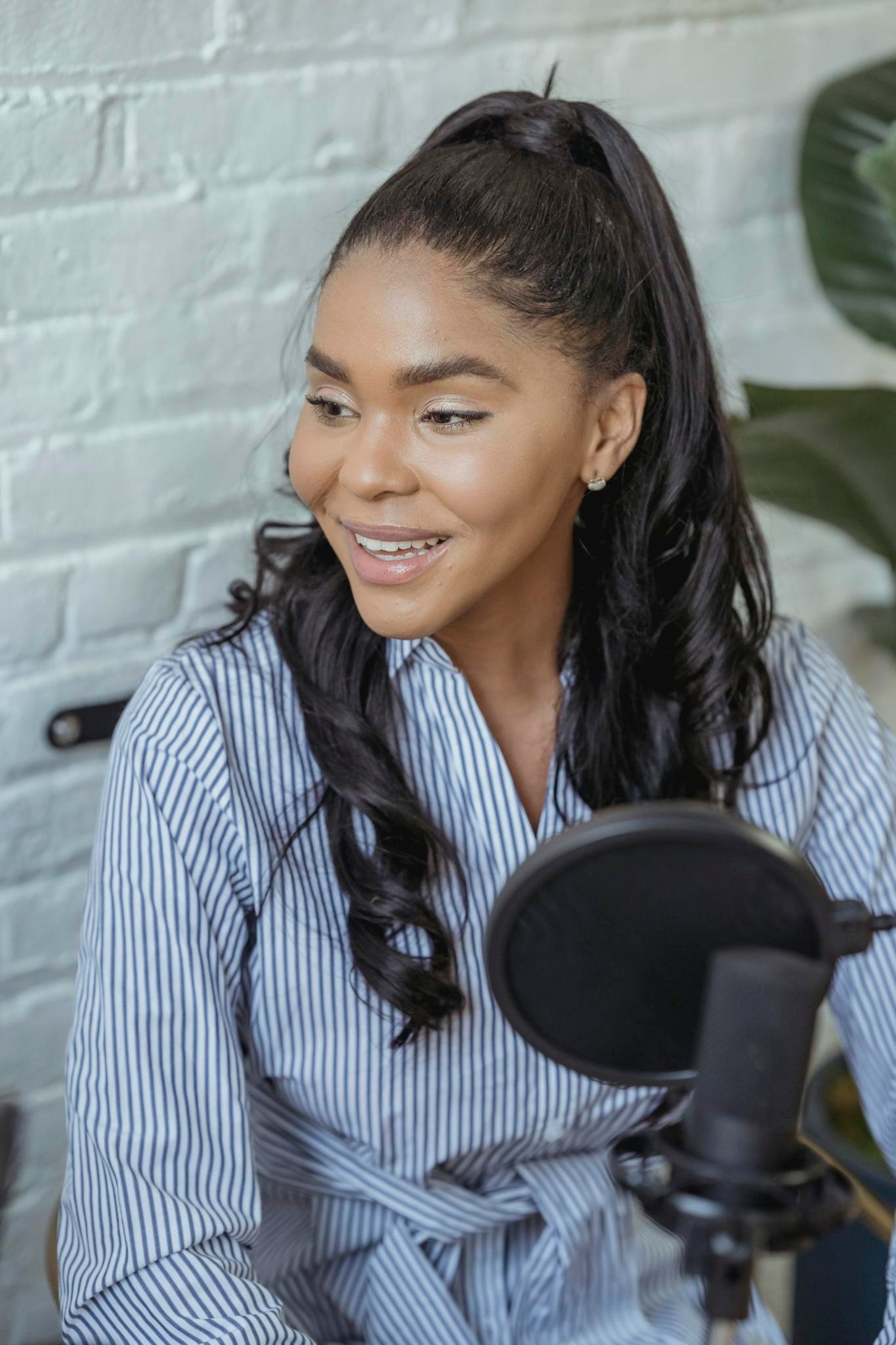 Cheerful African American female smiling and recording voice with microphone in contemporary broadcasting studio